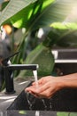 Woman washing her hands with pouring water from tap at stone sink in outdoor bathroom with tropical leaves Royalty Free Stock Photo