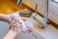 A woman is washing her hands with soap at the kitchen sink. Royalty Free Stock Photo