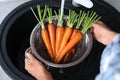 Woman washing ripe carrots in colander with running water over sink, closeup