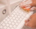 Woman washing white computer keyboard with a sponge with foam.