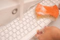 Woman washing white computer keyboard with a sponge with foam.