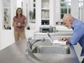 Woman Watching Bald Man Use Laptop In Kitchen Royalty Free Stock Photo