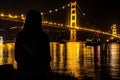 woman watching boats pass under a goldenlit suspension bridge at night