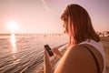 Woman watching mobile phone on the sea during sunset Royalty Free Stock Photo