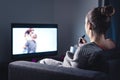 Woman watching romantic movie and eating ice cream. Sad lonely single girl streaming series or film on tv home at night.