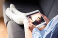 Woman watching tv series or movie stream with tablet on couch wearing cozy long socks. Girl streaming film with mobile device. Royalty Free Stock Photo