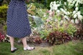 A woman waters flowers in her garden with a steel watering can.