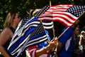 A Woman Waves Thin Blue Line and American Flags at a Conservative Rally