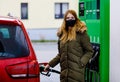 Woman wear medical mask at self-service gas station, hold fuel nozzle, refuel the car with petrol during corona virus Royalty Free Stock Photo