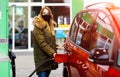 Woman wear medical mask at self-service gas station, hold fuel nozzle, refuel the car with petrol during corona virus Royalty Free Stock Photo