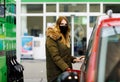 Woman wear medical mask at self-service gas station, hold fuel nozzle, refuel the car with petrol during corona virus Royalty Free Stock Photo