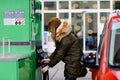 Woman wear medical mask at self-service gas station, hold fuel nozzle, refuel the car with petrol during corona virus Royalty Free Stock Photo