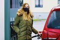 Woman wear medical mask at self-service gas station, hold fuel nozzle, refuel the car with petrol during corona virus Royalty Free Stock Photo