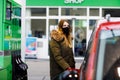 Woman wear medical mask at self-service gas station, hold fuel nozzle, refuel the car with petrol during corona virus Royalty Free Stock Photo