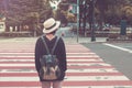Woman wear white weave hat and black overcoat. She standing on footpath and waiting for crossing the road. Royalty Free Stock Photo