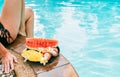 Woman weared swimsuit sitting on swimming pool side with plate of tropical fruits