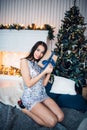 Woman wearing amazing shiny dress with a Christmas Gift on the Christmas interior background with a fir tree and Royalty Free Stock Photo