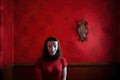 Woman wearing an anonymous mask standing against a red wallpapered. Generative AI