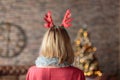 Woman wearing antler deer headband looking at decorated Christmas tree. Rear view