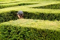 Woman wearing a baseball cap walks around lost in a giant labyrinth made of boxwood hedges