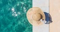 Woman wearing big summer sun hat relaxing on pier by clear turquoise sea. Royalty Free Stock Photo