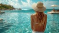 A woman in a bikini and hat stands in a pool gazing at the azure ocean Royalty Free Stock Photo