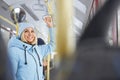 Woman wearing blue cap and winter jacket holding handle enjoying trip in bus.