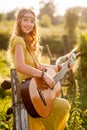 Woman wearing a bohemian style, playing a guitar on field at warm light of sunset Royalty Free Stock Photo