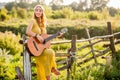 woman wearing a bohemian style, playing a guitar on field at sunset Royalty Free Stock Photo