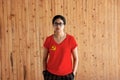 Woman wearing Chinese Communist Party flag color shirt and standing with two hands in pant pockets on the wooden wall background Royalty Free Stock Photo