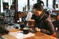 Woman wearing coat and making pour-over coffee with alternative method called Dripping.