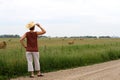 Woman wearing a cowboy hat looking a a field of hay bales.