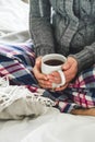 Woman wearing cozy pyjamas and gray cardigan drinking tea on a bed