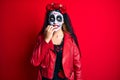 Woman wearing day of the dead costume over red looking stressed and nervous with hands on mouth biting nails