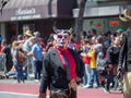 Woman wearing a devil mask and cracking a whip walks down the st