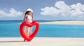 Woman holding a heart shape swimming float in a tropical beach