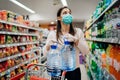 Woman wearing face mask buying bottled water in supermarket/drugstore with sold-out supplies.Prepper buying bulk supplies