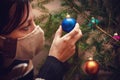 Woman wearing a face mask and is decoration a christmas tree with baubles or balls Royalty Free Stock Photo