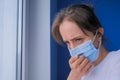 Woman with face mask suffering from coughing, looking out of window - close up Royalty Free Stock Photo
