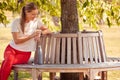 Woman Wearing Fitness Clothing Sitting On Seat Under Tree Checking Activity Monitor On Smartwatch