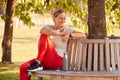 Woman Wearing Fitness Clothing Sitting On Seat Under Tree Checking Activity Monitor On Smartwatch