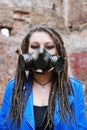 Woman wearing gas mask with spikes in blue jacket and black dress standing in ruined building is looking at camera Royalty Free Stock Photo