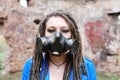 Woman wearing gas mask with spikes in blue jacket and black dress standing in ruined building is looking at camera Royalty Free Stock Photo