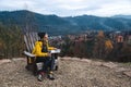 Woman wearing glasses and yellow jacket working on laptop outdoors surrounded by beautiful nature, forest and mountains. Workation Royalty Free Stock Photo