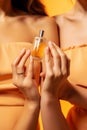 Woman wearing a handbag, filling a bottle with a liquid skin care product, in the style of light orange and light gold