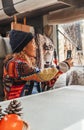 Woman wearing hat and pacwork sweater sitting in camper taking photos with cell phone looking out the window. Relaxation and