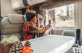 Woman wearing hat and pacwork sweater sitting in camper taking photos with cell phone looking out the window. Relaxation and