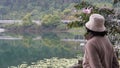 Woman wearing hat, standing alone from behind looking at the view of the lake with beautiful bridge and tree reflections