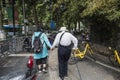 A woman wearing a hat and a walking stick wearing a white coat and a humpbacked elderly woman walking in the street