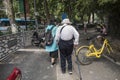 A woman wearing a hat and a walking stick wearing a white coat and a humpbacked elderly woman walking in the street